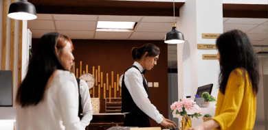Photo de l'accueil d'un hôtel, un professionnel de l'hôtellerie - restauration passé par une formation ifocop travaille, concentré, sous le regard de deux clientes.